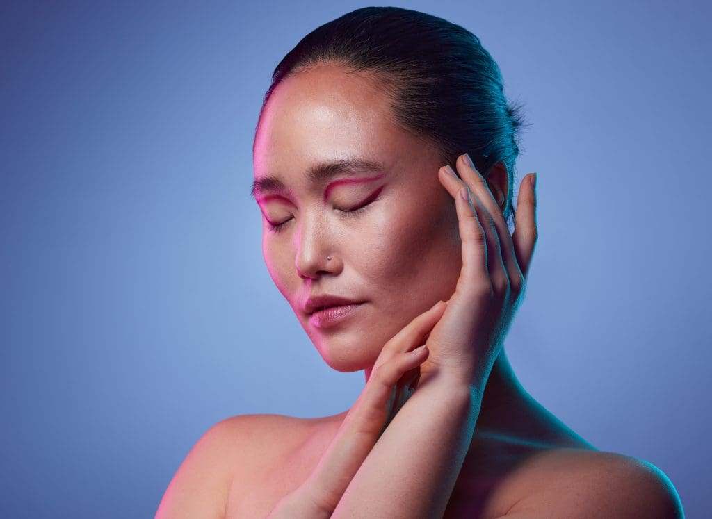 a woman posing with her hands on the side of her face against a purple background, showing that marshmallow root extract can do wonders for the skin
