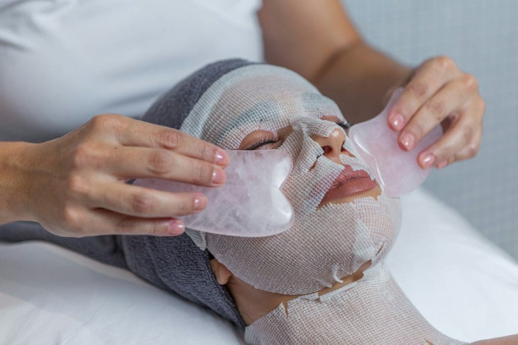 face of woman receiving gua sha facial massage treatment by beautician in health spa