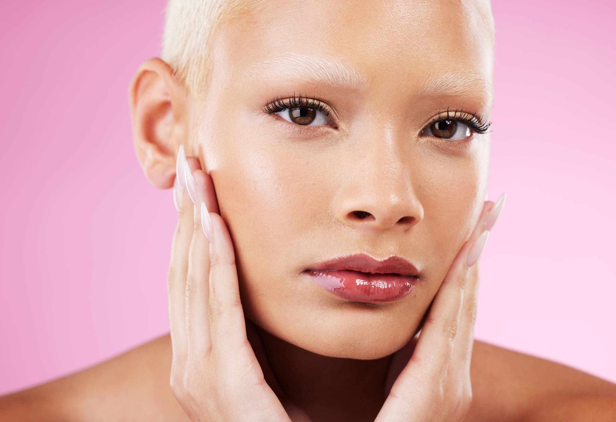 a woman with a bright complexion against a pink background, highlighting the fact that a vitamin c facial works