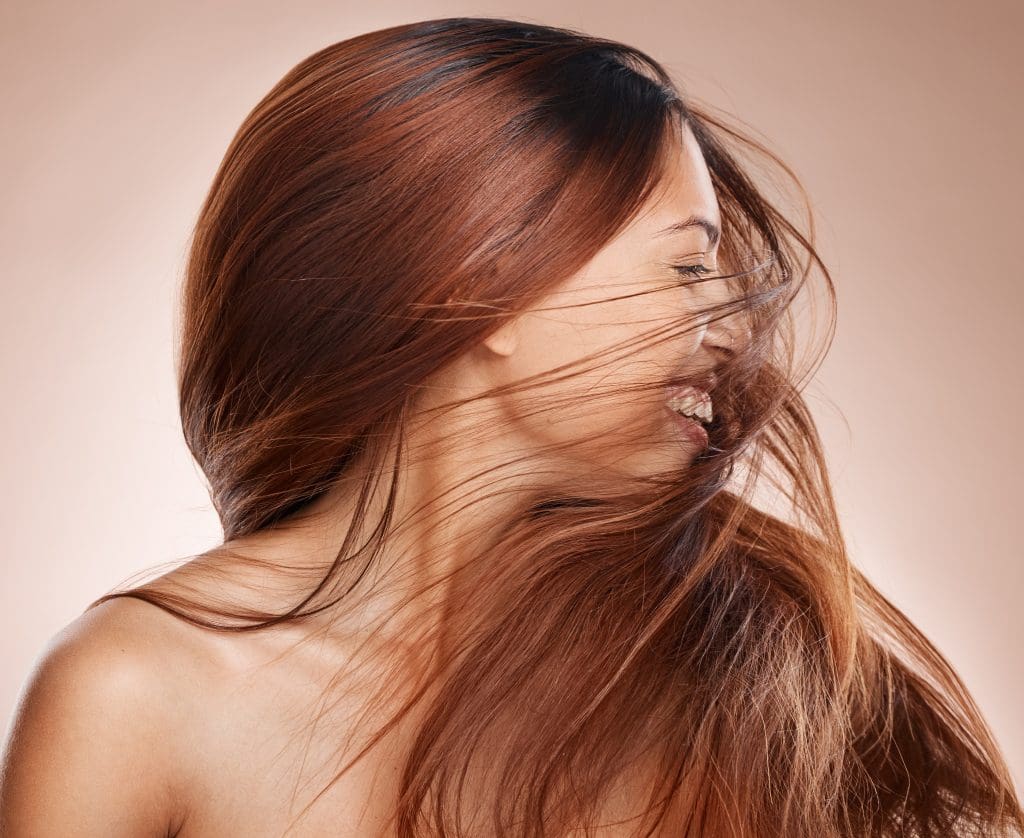a woman happily shaking her hair wondering "is red light therapy good for hair"