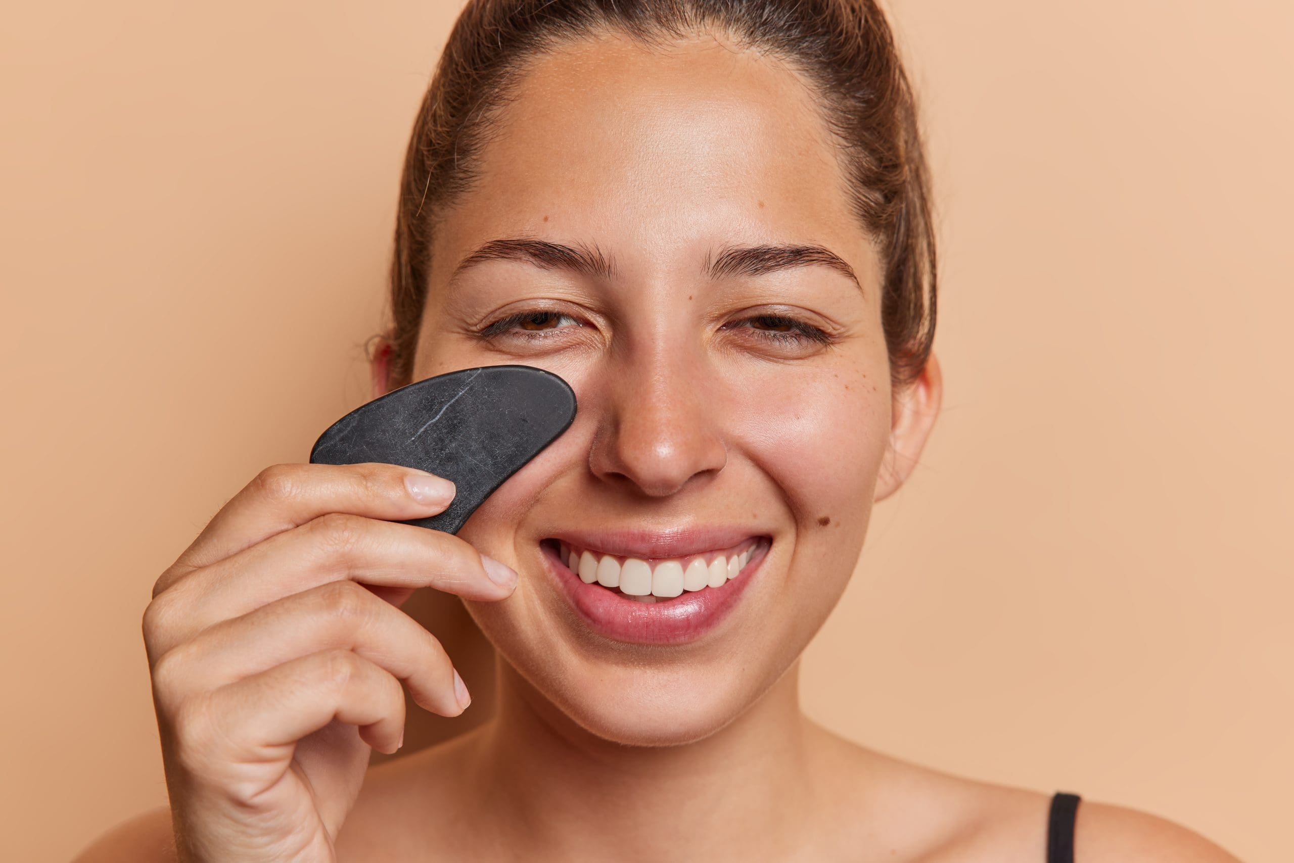 a smiling woman with a gua sha stone on her face, using gua sha and blood circulation