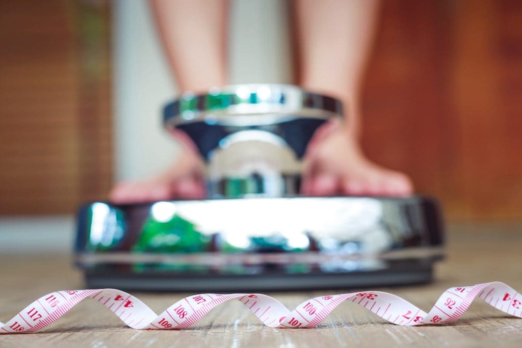 stepping on a scale with a waist tape measure in the foreground , showing the power of red light therapy weight loss