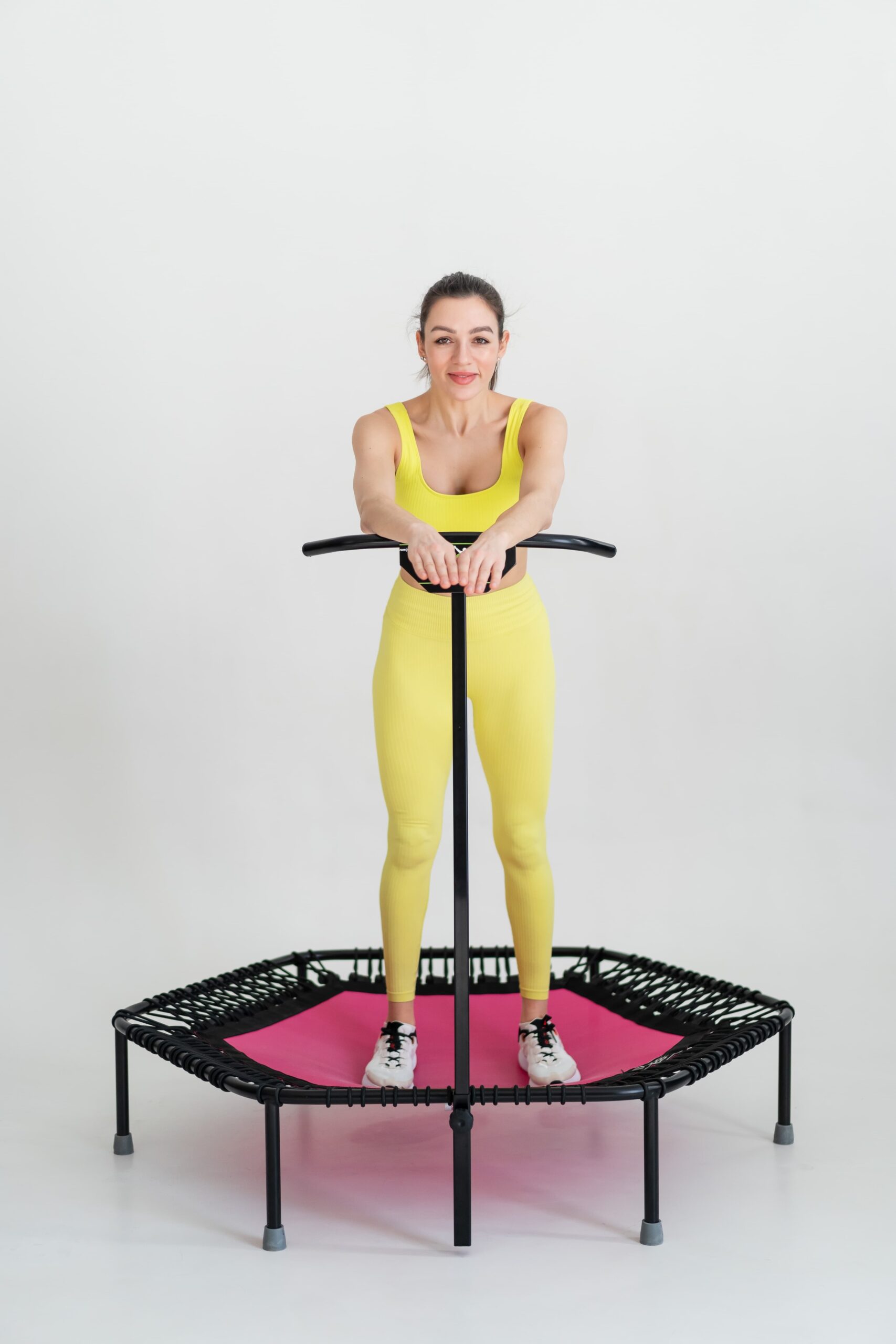 Woman using rebounder therapy for arthritis with stability bar support in a wellness studio