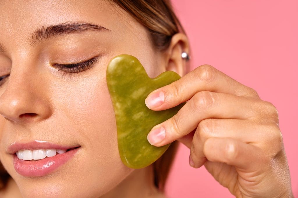 a woman using gua sha to reduce her facial puffiness