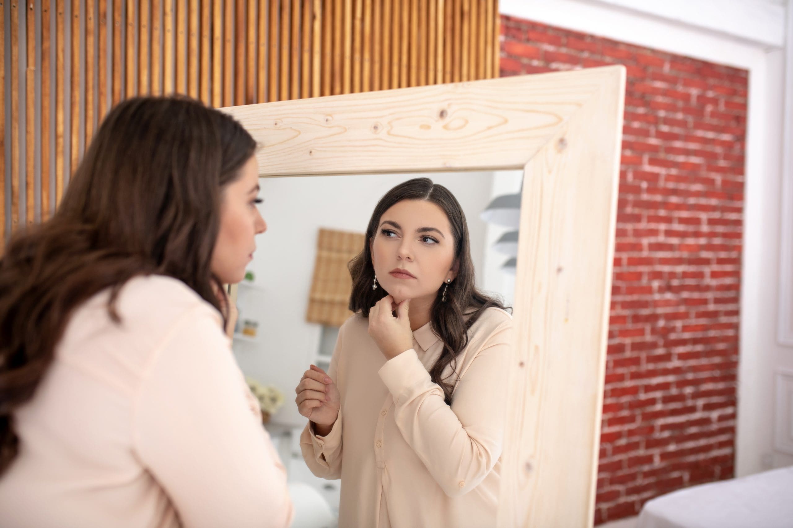a woman looking at her face in the mirror wondering if gua sha can help skin sagging