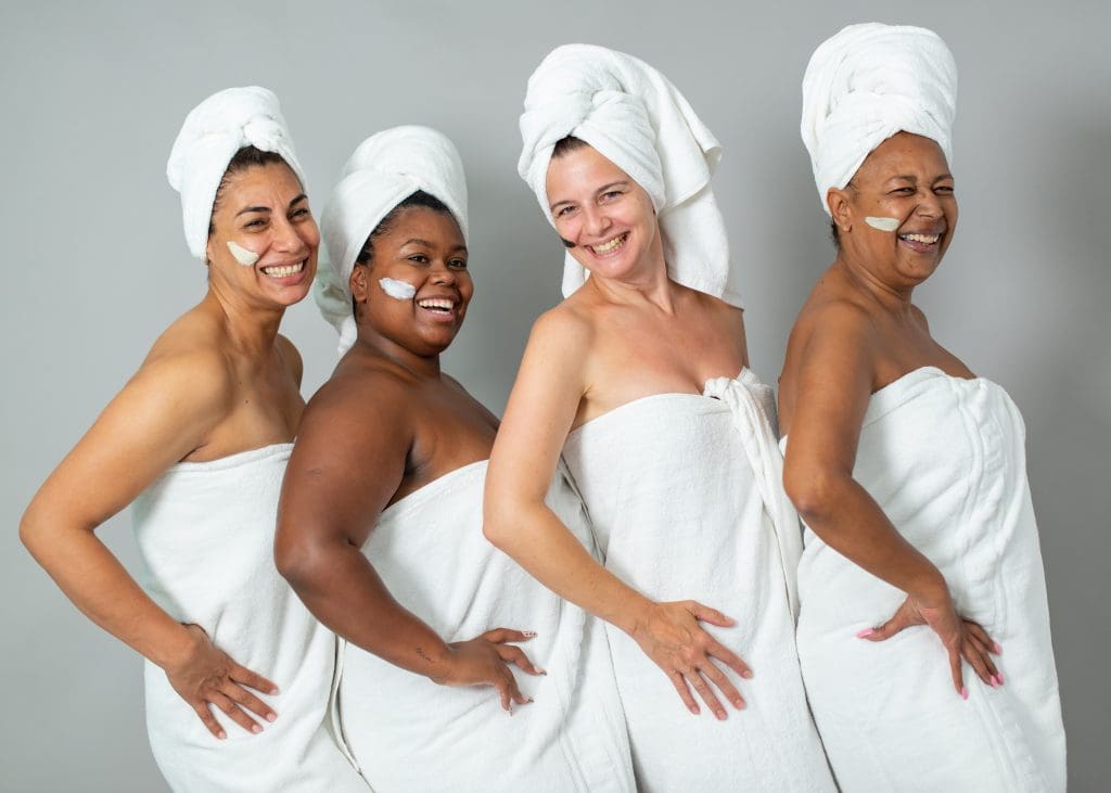 4 women standing together wrapped in towels celebrating Self-Improvement Month by having a spa day
