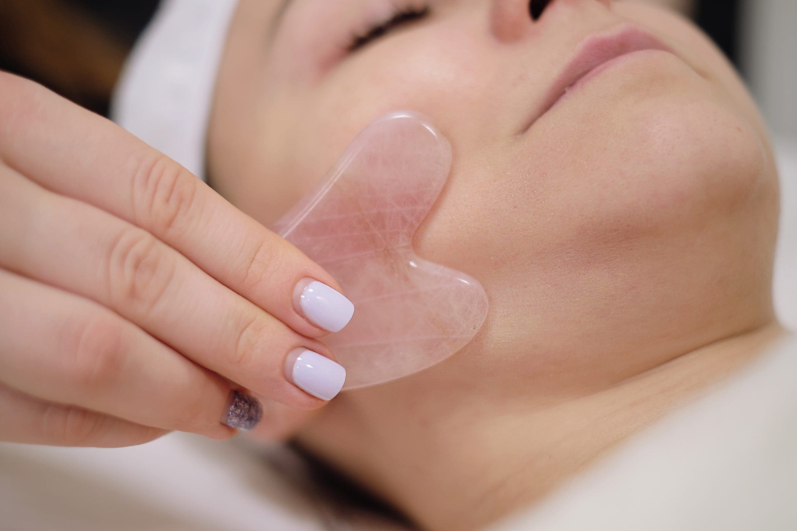 a woman having a gua sha facial massage up close, begging the question "how often should i use gua sha?"