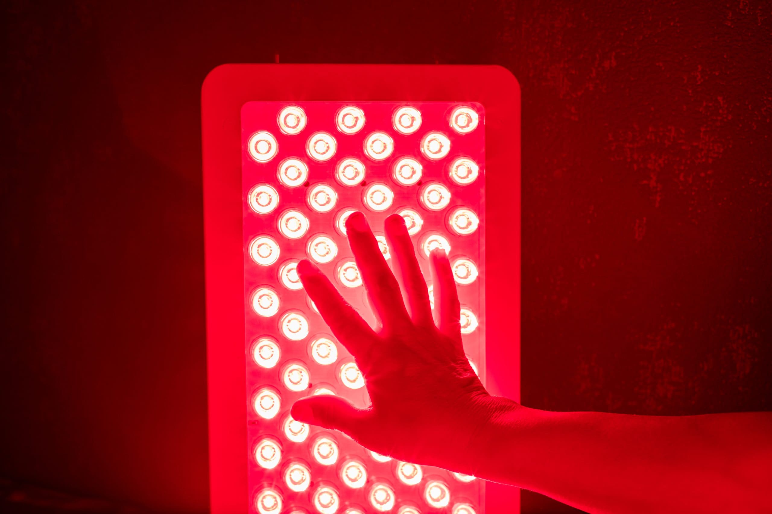 a hand pressing on a red light panel to show rebounder and red light therapy can enhance your mood