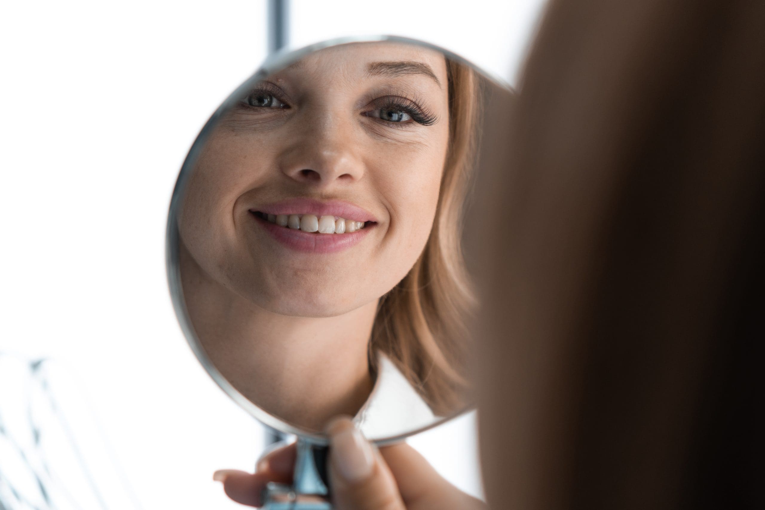 a woman smiling at herself in the mirror after using peptides and endospheres therapy to keep a toned face after weight loss