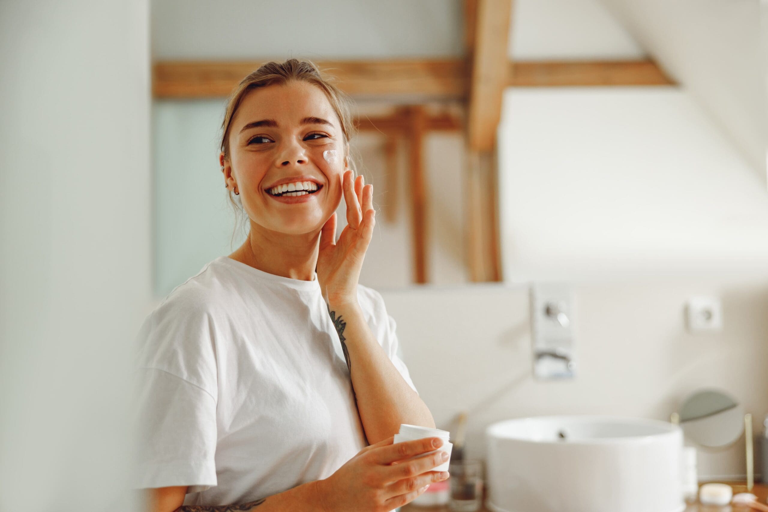 Person doing morning skincare with a calm expression in a sunlit bathroom.